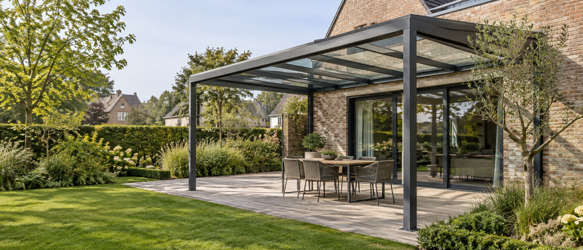 Glazen terrasoverkapping aan een woning, met een eettafel en een groene tuin.